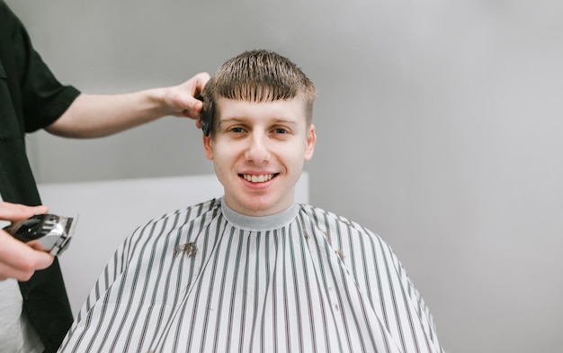 Coiffeur avec un peigne et une tondeuse à cheveux dans ses mains fait une coupe de cheveux pour un client souriant