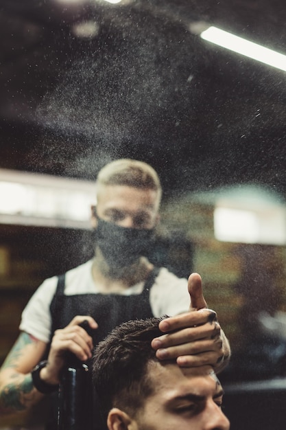 Coiffeur professionnel appliquant un spray sur les cheveux du client après le coiffage