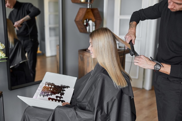 Coiffeur professionnel est en train de peigner les cheveux d'une belle femme blonde caucasienne dans un salon moderne