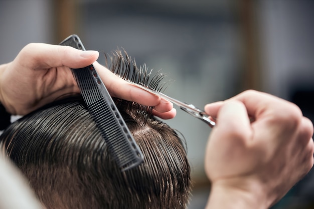 coiffeur professionnel faisant une coupe de cheveux au jeune homme à l'aide de ciseaux et d'un peigne au salon de coiffure