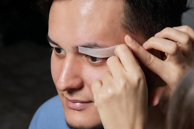 Coiffeur professionnel faisant la procédure de filetage et corrigeant la forme des sourcils au jeune client masculin avec une pince à épiler dans le salon de coiffure Coiffeur au travail Concept de soins des sourcils Plumer les sourcils