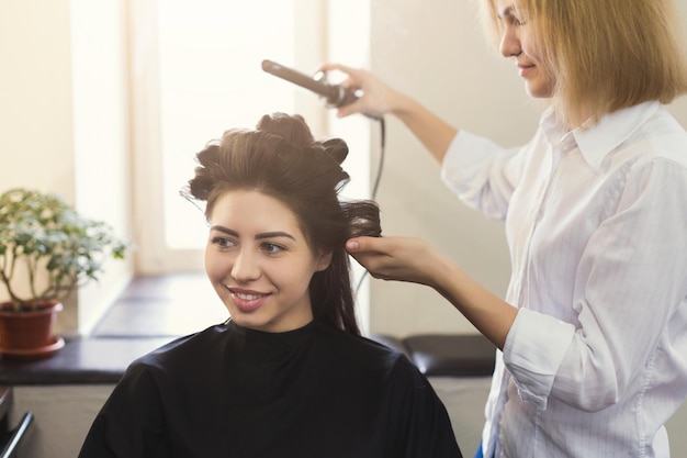 Un coiffeur professionnel fait de belles boucles avec un bigoudi sur des cheveux bruns dans un salon de beauté