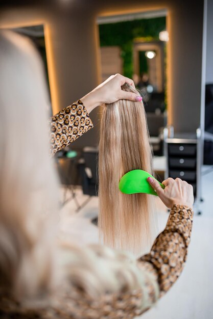 Le coiffeur professionnel prépare les cheveux blonds pour les extensions et les peigne dans un salon de beauté