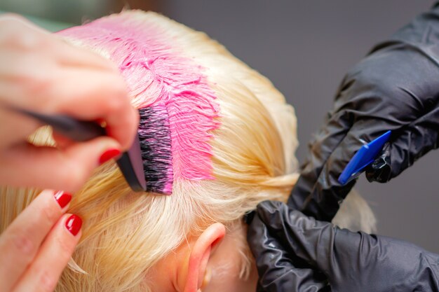 Coiffeur professionnel teint les cheveux de la jeune femme en couleur rose