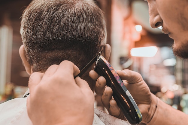 Le coiffeur de salon effectue professionnellement la coupe de cheveux pour l'homme Les mains du coiffeur avec une tondeuse à cheveux