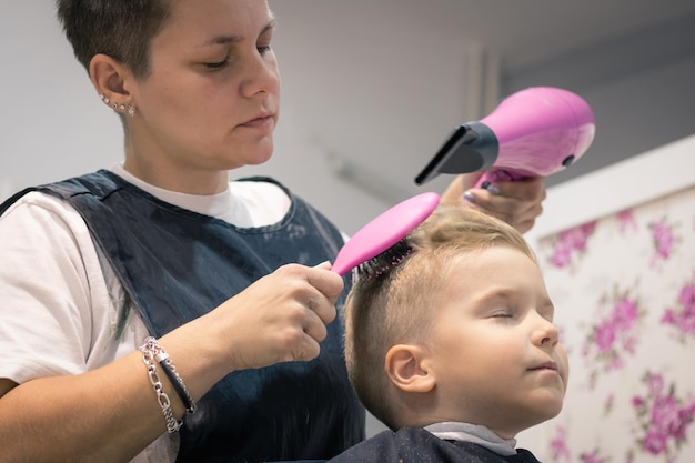 Un coiffeur sèche les cheveux d'un garçon assis sur une chaise au magasin.