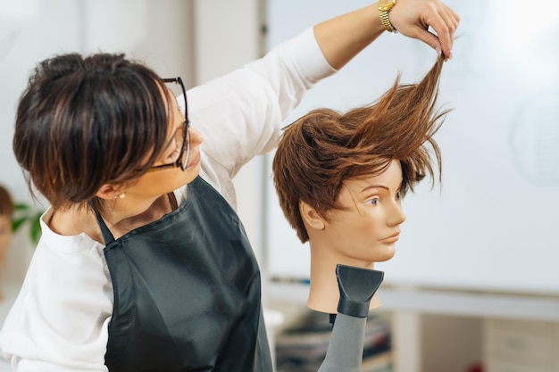 Photo un coiffeur avec le sèche-cheveux en main expliquant les techniques de coiffure en utilisant la tête d'un mannequin