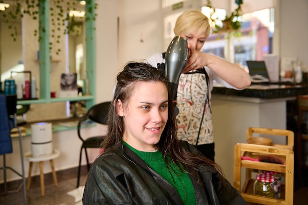 Le coiffeur sèche et coiffe les cheveux avec un sèche-cheveux dans le salon de beauté