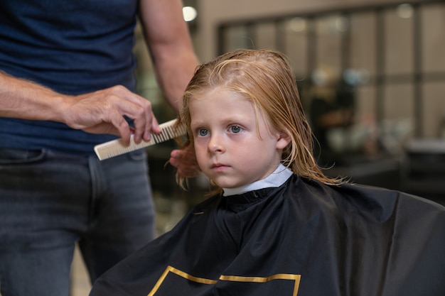 Photo coiffeur styliste peignant les cheveux du garçon avant de couper