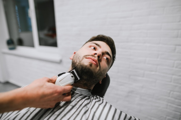 Le coiffeur taille la barbe d'un bel homme avec une tondeuse à la main