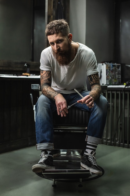 coiffeur avec des tatouages sur ses bras tenant des instruments de barbier