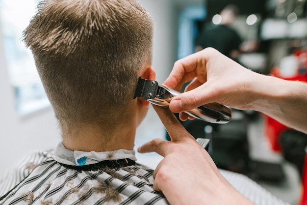 Coiffeur avec tondeuse dans ses mains coupe les cheveux d'un jeune homme