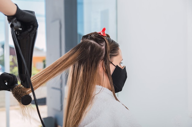 Coiffeur utilisant un sèche-cheveux sur cheveux longs dans le salon de beauté.