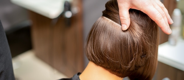 Coiffeur vérifie la coiffure brune courte d'une jeune femme dans un salon de beauté