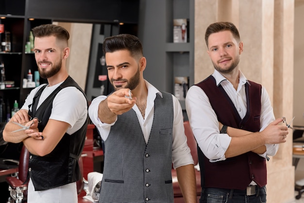 Coiffeurs posant, barbier barbu pointant avec des ciseaux à la caméra et un clin de œil.