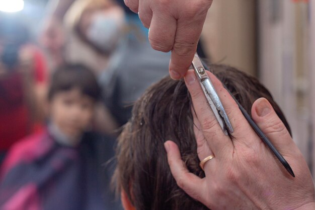 Une coiffeuse coupe les cheveux d'un garçon avec des ciseaux