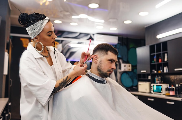 Une coiffeuse coupe les cheveux d'un homme dans un salon de coiffure Salon de coiffure professionnel pour hommes Barbershop