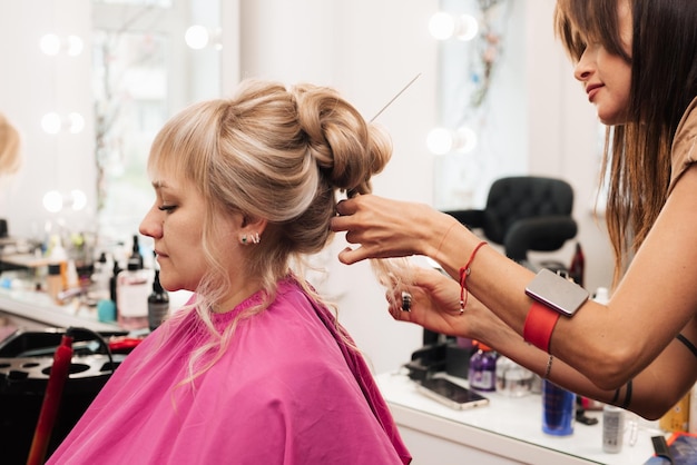 Une coiffeuse fait une coiffure de clients pour la célébration en épinglant les mèches avec des épingles à cheveux et des épingles à cheveux