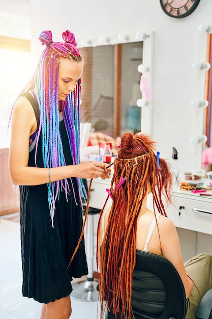 Coiffeuse fille avec des tresses afro colorées tisse des dreadlocks au gingembre femme élégante thérapie professiona...