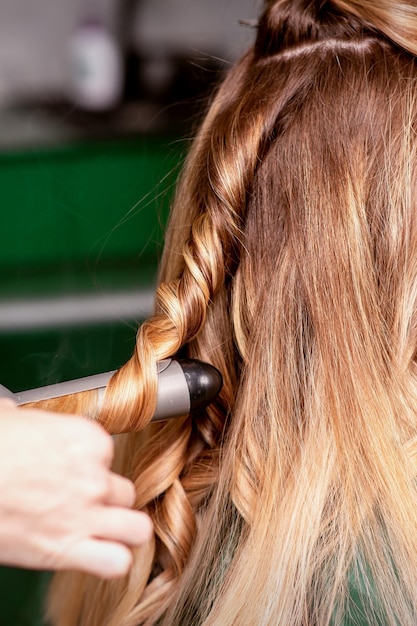 La coiffeuse frise les cheveux d'une jeune femme caucasienne aux cheveux bruns dans un salon de beauté