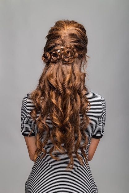 Coiffure de boucles de vague. Coiffure sur femme cheveux brun rouge aux cheveux longs sur fond gris.