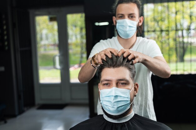 Coiffure à la cire pour un homme barbu dans un masque médical. Le travail du salon de coiffure en quarantaine coronavirus covid-19.