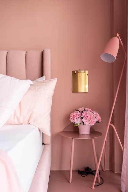 Coin de chambre rose confortable avec lit en tissu velours rose bébé décoré d'une couverture, d'oreillers et d'un lampadaire rose avec un mur peint en rose bicolore