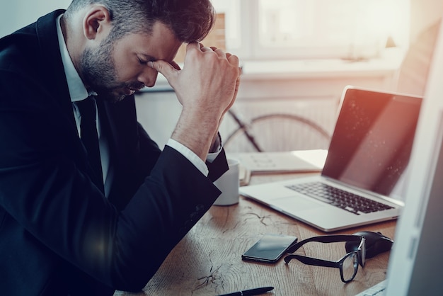 Coincé au bureau. Jeune homme fatigué en tenue de soirée massant le nez alors qu'il était assis au bureau
