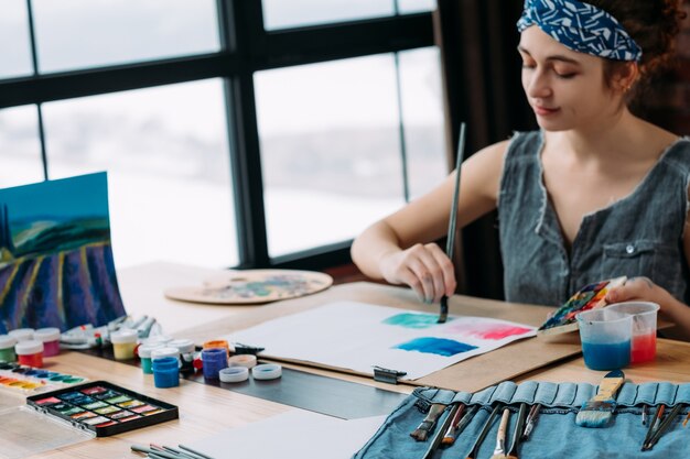 École d'art. Inspiré jeune artiste féminin peinture paysage dans un studio moderne. Fenêtre floue.