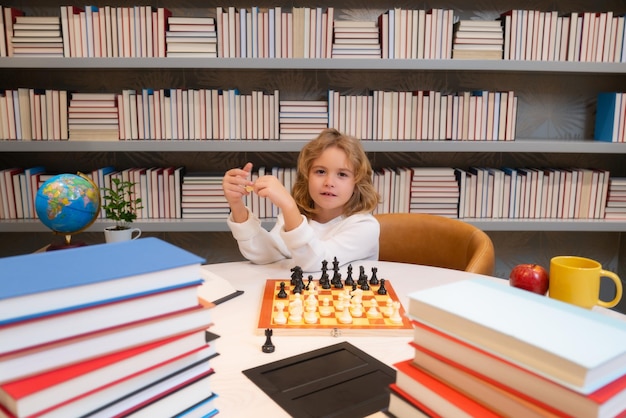 École d'échecs Un enfant concentré joue aux échecs Un enfant intelligent joue aux échecs dans la bibliothèque près des étagères Concept éducatif Garçon pensant aux échecs Le concept d'apprentissage et de croissance des enfants