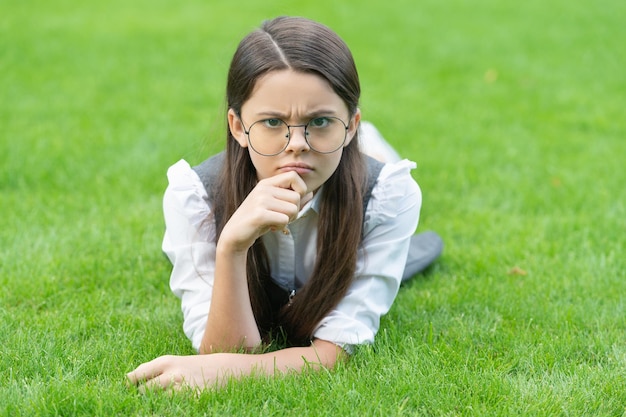 École et éducation Frown adolescente dans des verres allongé sur l'herbe après l'école retour à l'école