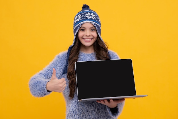 École d'hiver Une écolière adolescente tient un ordinateur portable dans des vêtements d'automne sur fond de studio isolé jaune Visage heureux émotions positives et souriantes d'une adolescente