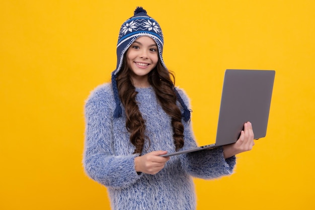 École d'hiver Une écolière adolescente tient un ordinateur portable dans des vêtements d'automne sur fond de studio isolé jaune Visage heureux émotions positives et souriantes d'une adolescente