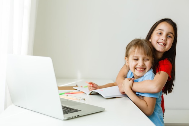 École en ligne sympa. Les enfants étudient en ligne à la maison à l'aide d'un ordinateur portable. Joyeuses jeunes filles utilisant un ordinateur portable pour étudier via un système d'apprentissage en ligne. Formation à distance ou à distance