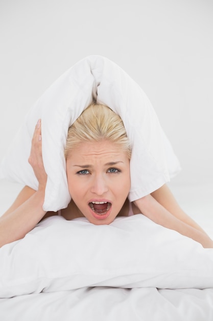 Photo en colère jeune femme couvrant les oreilles avec oreiller dans son lit