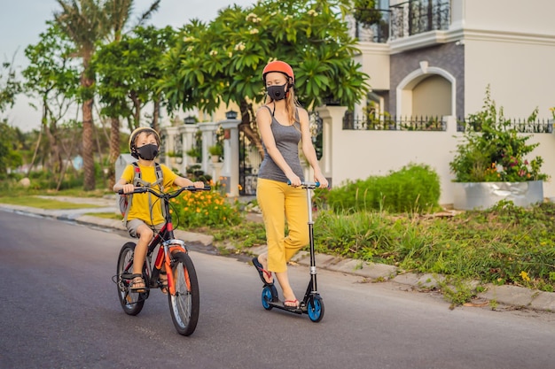 Écolier actif garçon et sa mère en masque médical et casque de sécurité faisant du vélo avec sac à dos sur