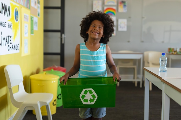 Écolier afro-américain souriant tenant un récipient avec un symbole de recyclage