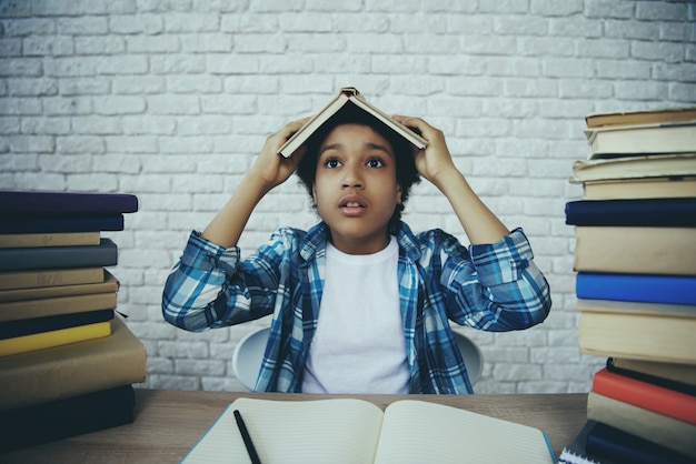 Écolier afro-américain tient un livre sur la tête.