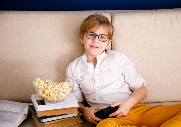 Écolier blond avec des lunettes joue à des jeux vidéo, tient une manette de jeu