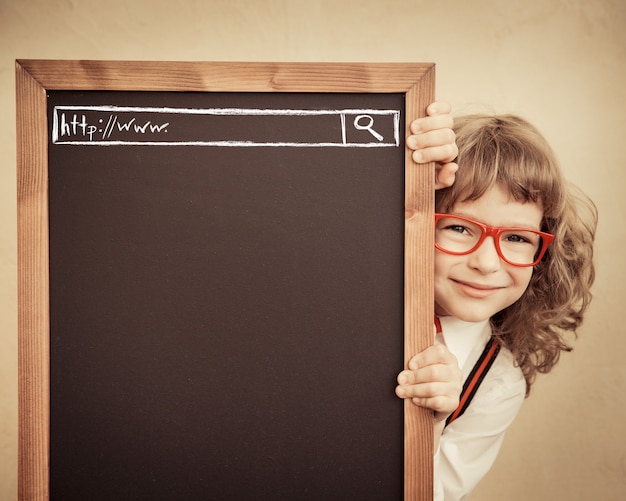 Écolier en classe. Enfant heureux tenant le tableau noir vierge. Notion d'éducation