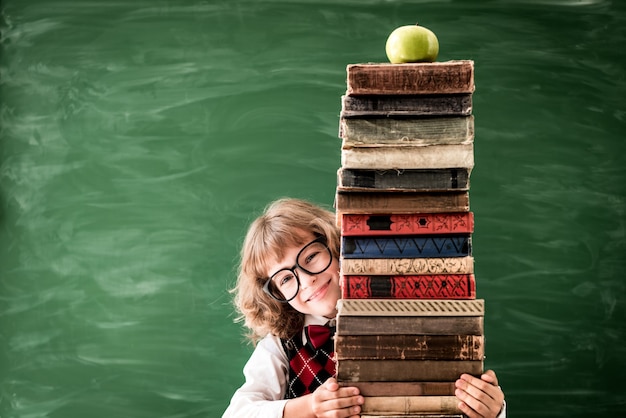 Écolier en classe. Heureux enfant tenant des livres contre le tableau vert. Notion d'éducation