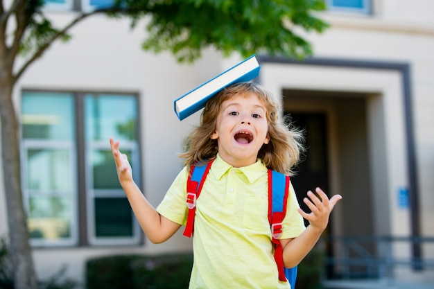 Écolier drôle excité avec livre à l'école.