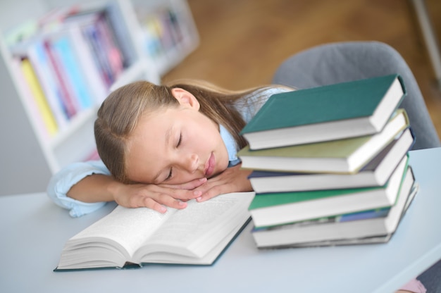 Écolier épuisé allongé les yeux fermés sur le bureau avec des livres dans une bibliothèque publique