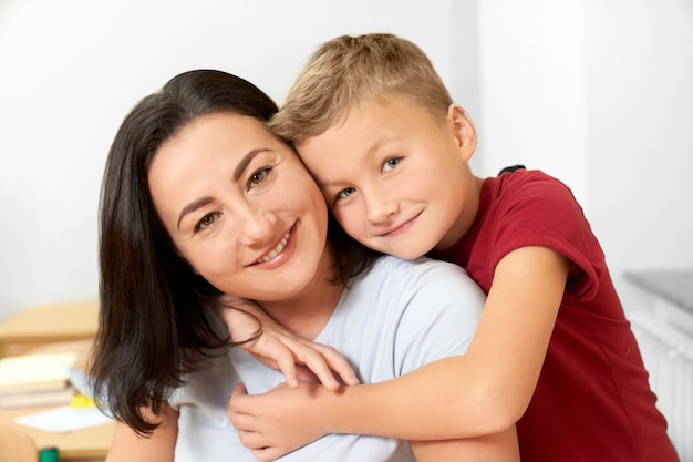 Écolier étreignant la mère, souriant, regardant la caméra.