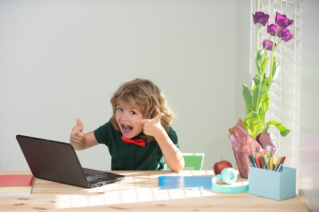 Écolier faisant ses devoirs excité petit garçon apprend avec un ordinateur portable dans la salle d'étude