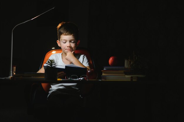 Écolier faisant ses devoirs à table dans sa chambre.