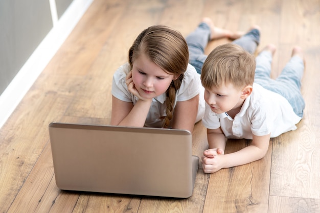 Écolier et fille étudient à la maison avec un ordinateur portable numérique et font leurs devoirs scolaires.