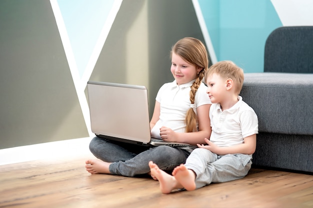 Écolier et fille étudient à la maison avec un ordinateur portable numérique et font leurs devoirs scolaires.