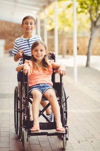 Écolier heureux poussant une fille en fauteuil roulant