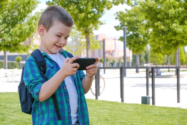 Écolier heureux regardant l'écran du smartphone et souriant, appel vidéo, jeux en ligne sur téléphone intelligent